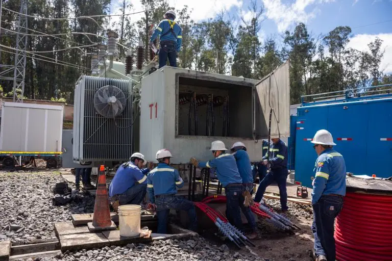 Trabajadores de mantenimiento eléctrico realizan tareas de conexión de cables de alta tensión en un transformador de potencia en una subestación eléctrica.